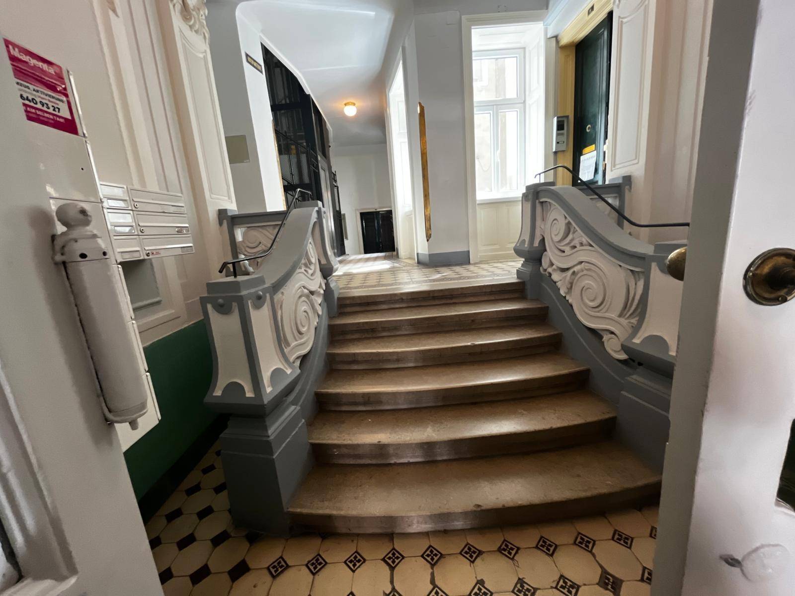 Historisches Treppenhaus mit kunstvollen Geländern und gemusterten Fliesen im Eingangsbereich.