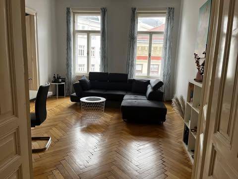 Geräumiges Wohnzimmer mit dunklem Sofa, Fischgrätparkett und hohen Fenstern.