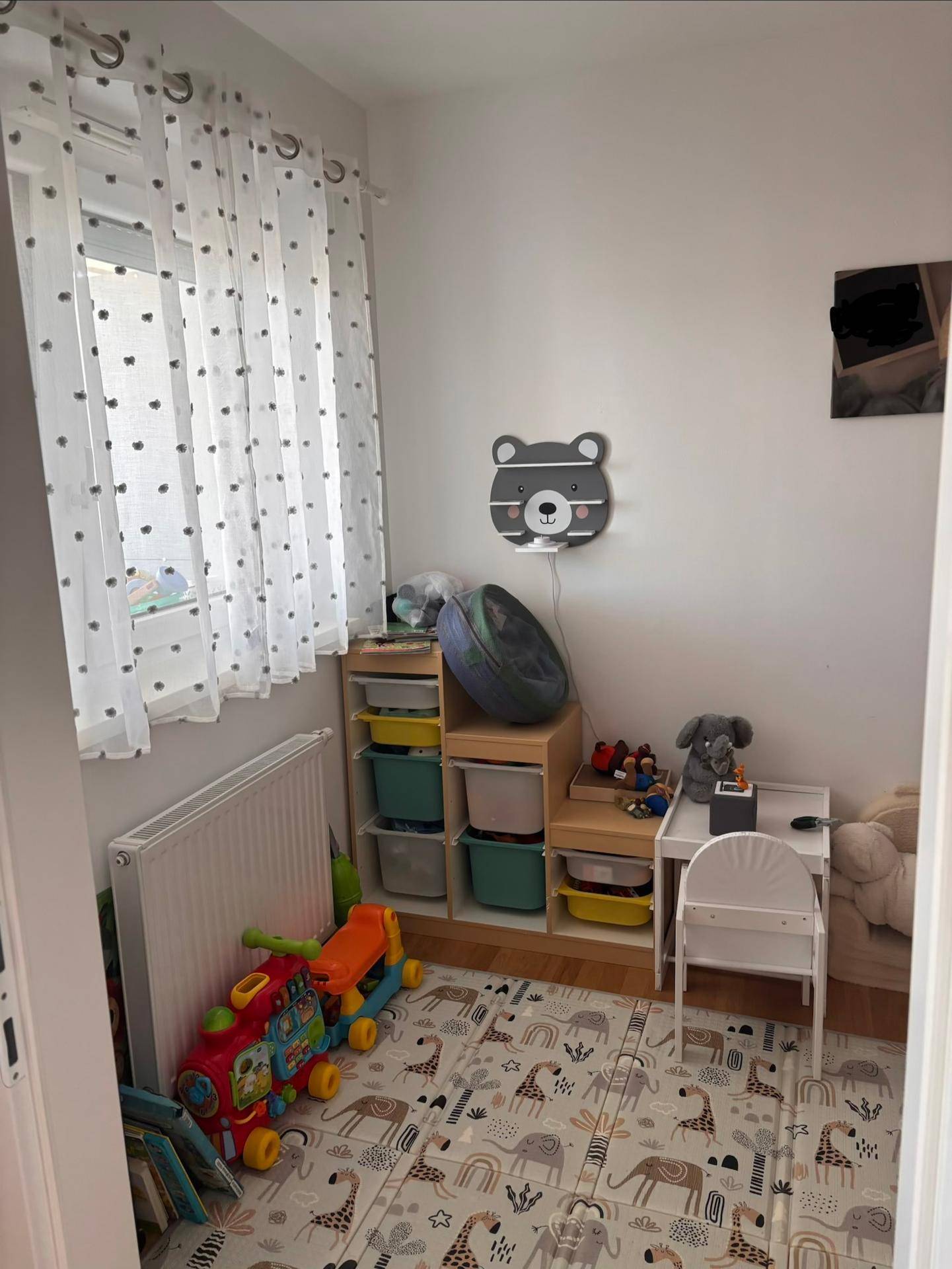Helles Kinderzimmer mit Spielteppich, praktischen Aufbewahrungsmöbeln und Fenster.