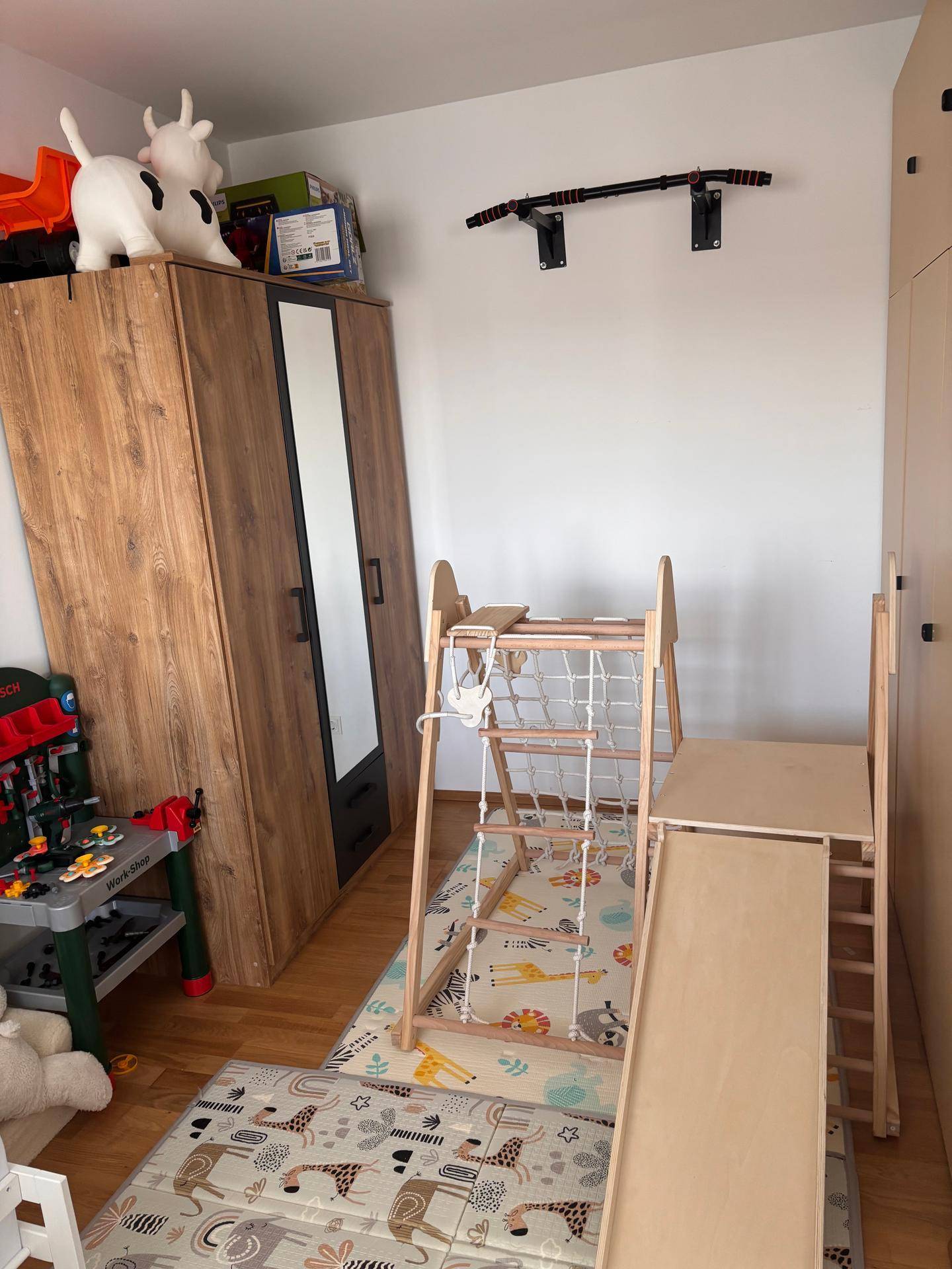 Kinderzimmer mit Spielgeräten aus Holz, Kleiderschrank und Holzboden.