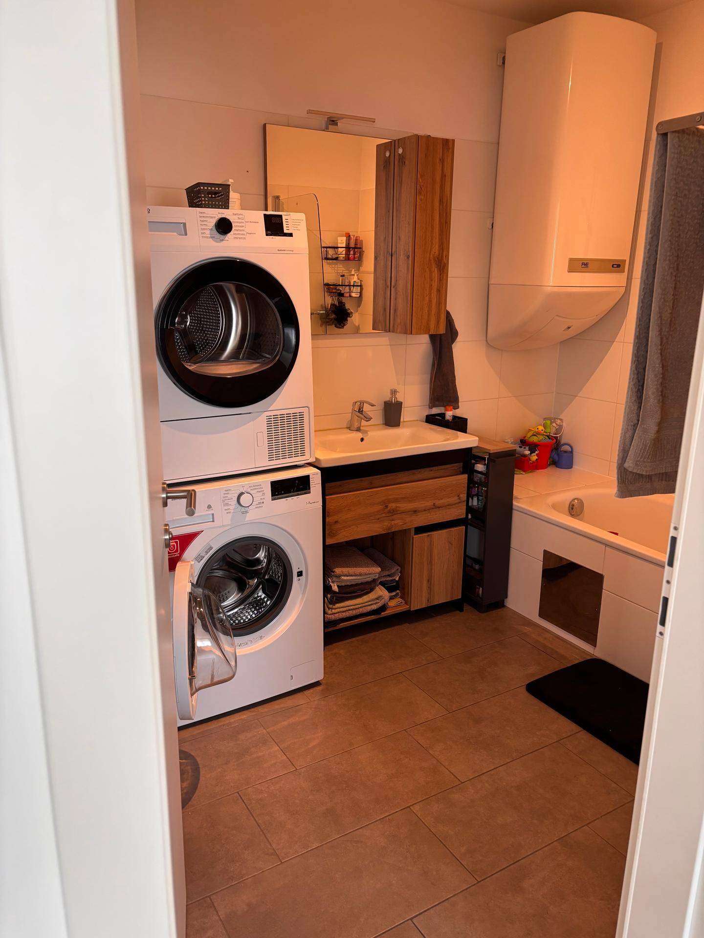 Funktionales Badezimmer mit Waschmaschine, Trockner, Badewanne und Holzwaschtisch.