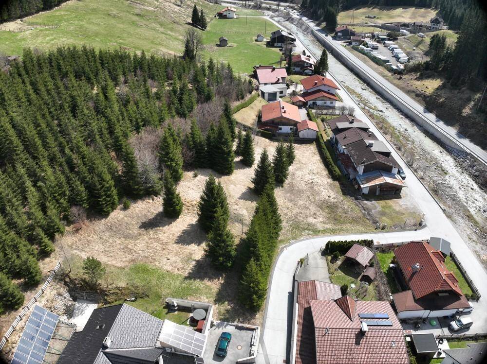Luftbild des Dorfes im Tal, mit Häusern entlang eines Flusses und bewaldeten Hängen.