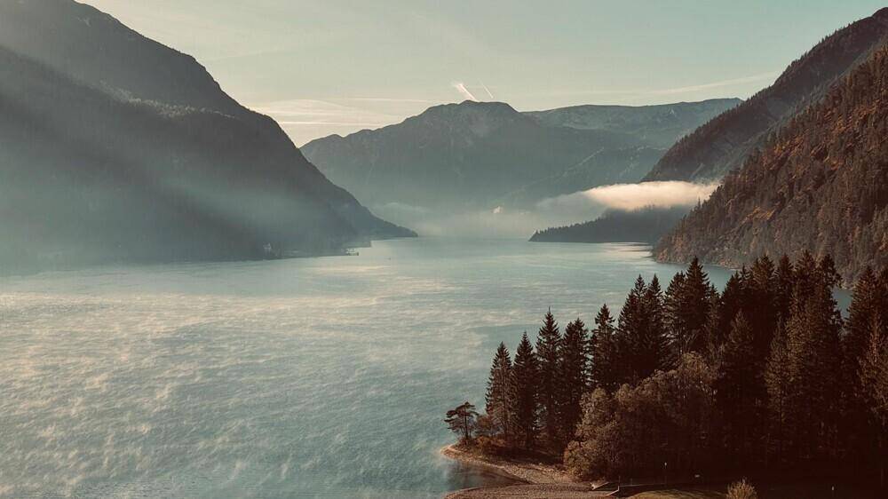 Malerische Landschaft mit einem See umgeben von Bergen und Nadelbäumen bei Sonnenaufgang.
