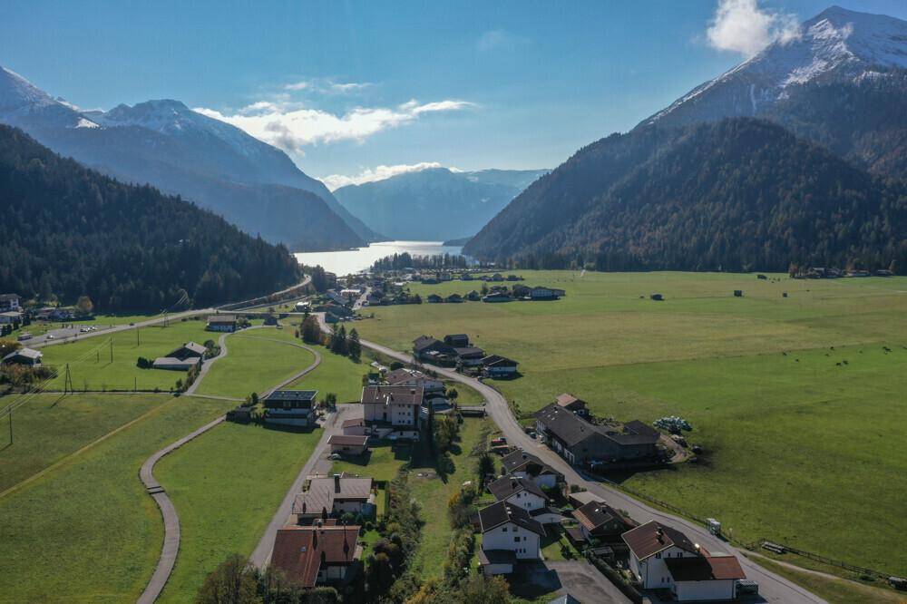 Luftaufnahme eines malerischen Dorfes am Seeufer, umgeben von majestätischen Bergen und grünen Feldern.