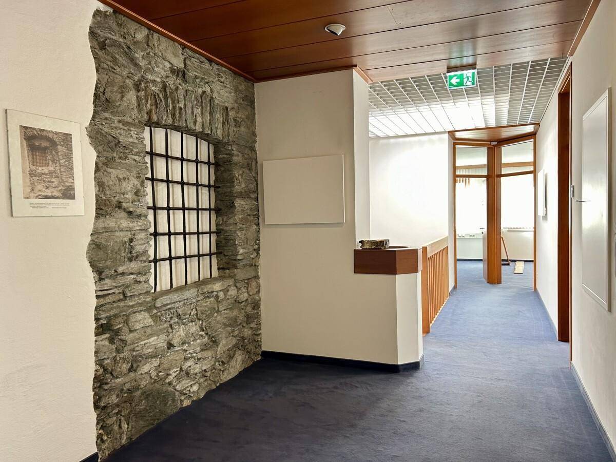 Flur mit blauem Teppichboden, Holztäfelung und einer rustikalen Steinwand mit Gitterfenster.