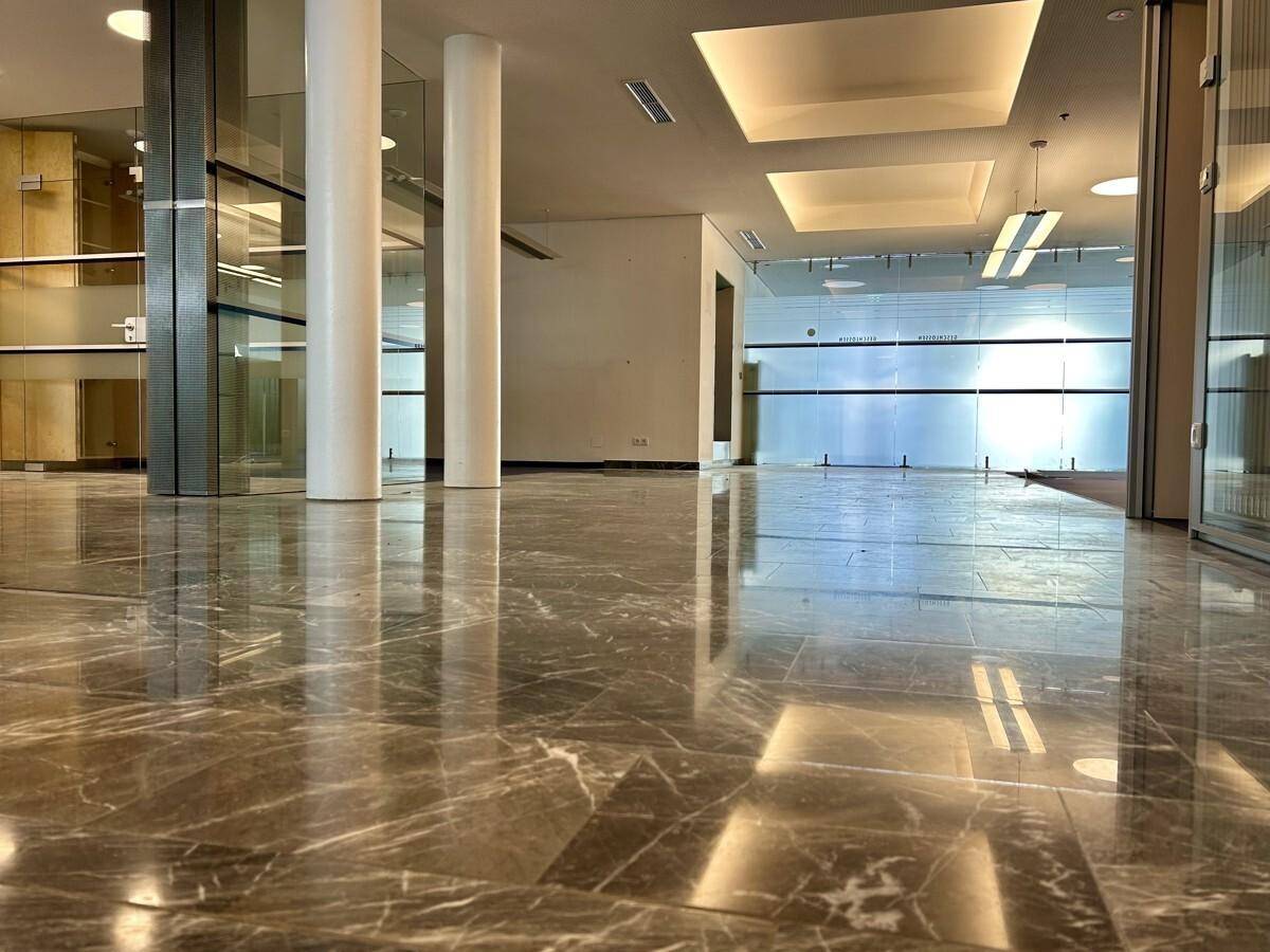 Weitläufiger Bürobereich mit glänzendem Marmorboden, Säulen und modernen Deckenleuchten.