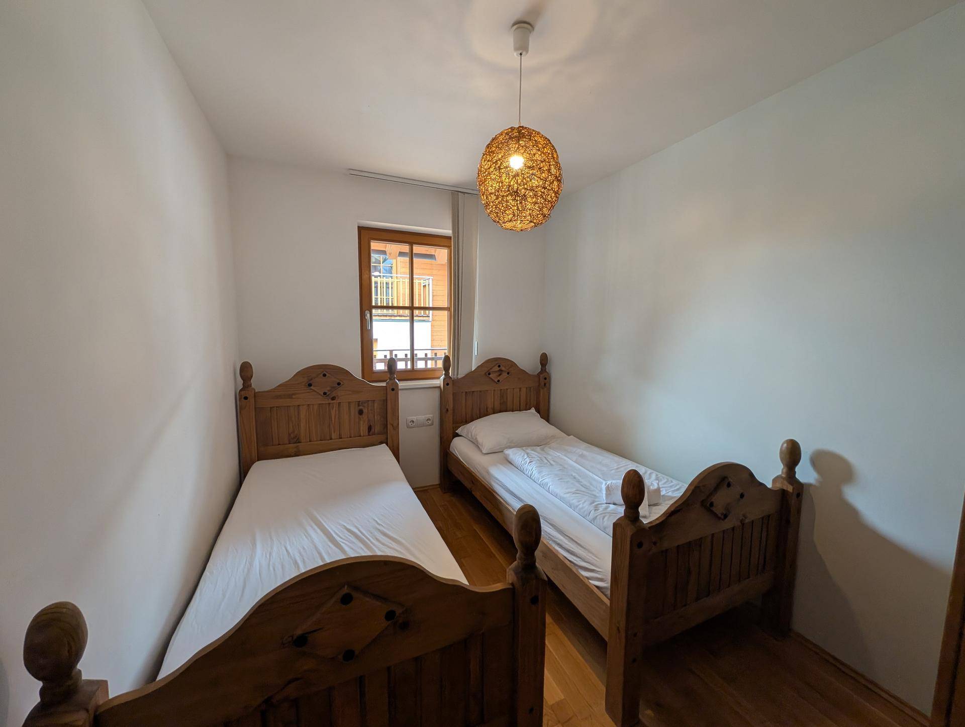 Zweites Schlafzimmer mit zwei Einzelbetten aus Holz und einem Fenster, das für Helligkeit sorgt.