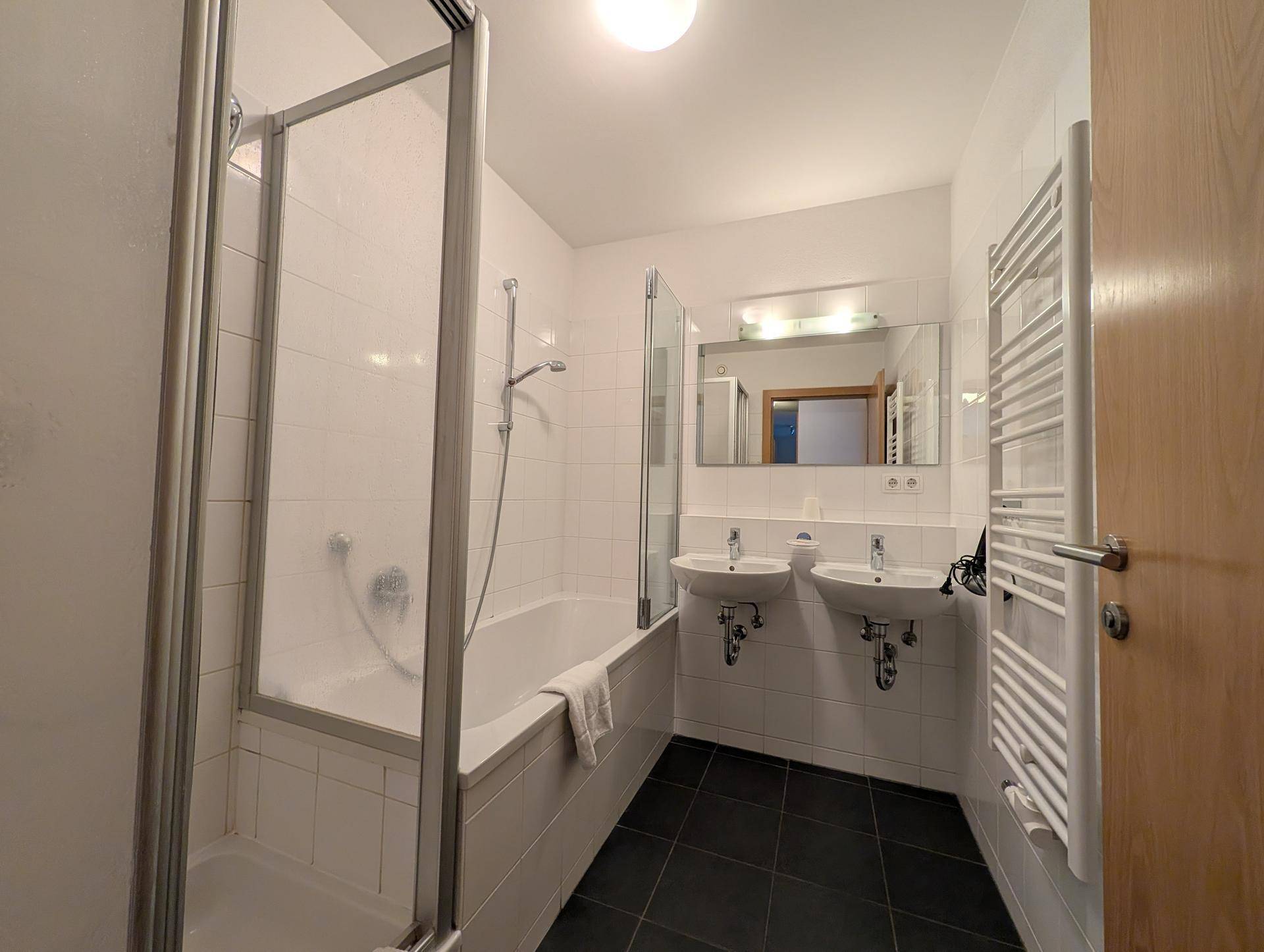 Modernes Badezimmer mit Badewanne, Duschabtrennung, Doppelwaschbecken und Handtuchheizkörper.