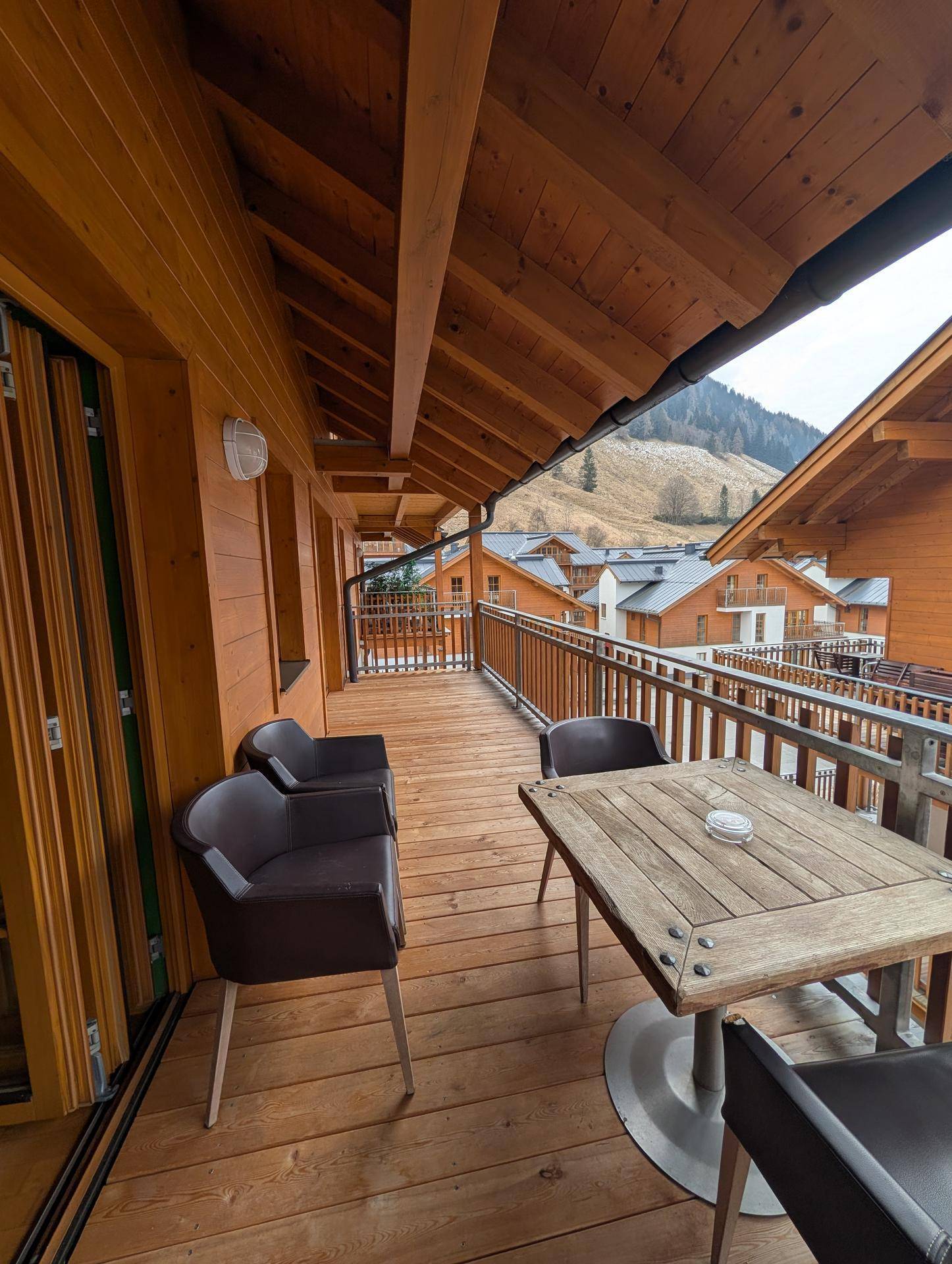 Geräumiger Holzbalkon mit Sitzgelegenheiten und einem Tisch, der einen schönen Blick auf die Berge bietet.