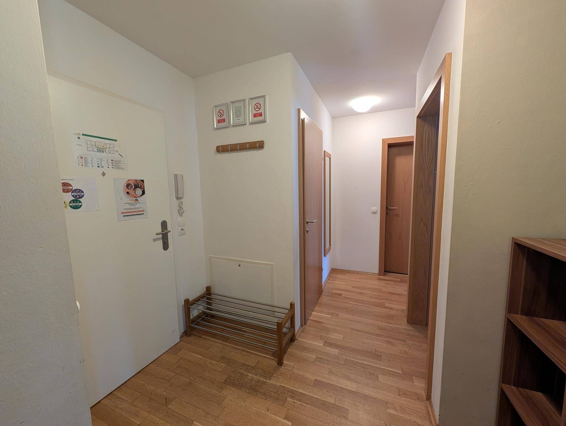 Heller Eingangsbereich mit Holzboden, Garderobe und Schuhregal, der zu den weiteren Räumen führt.