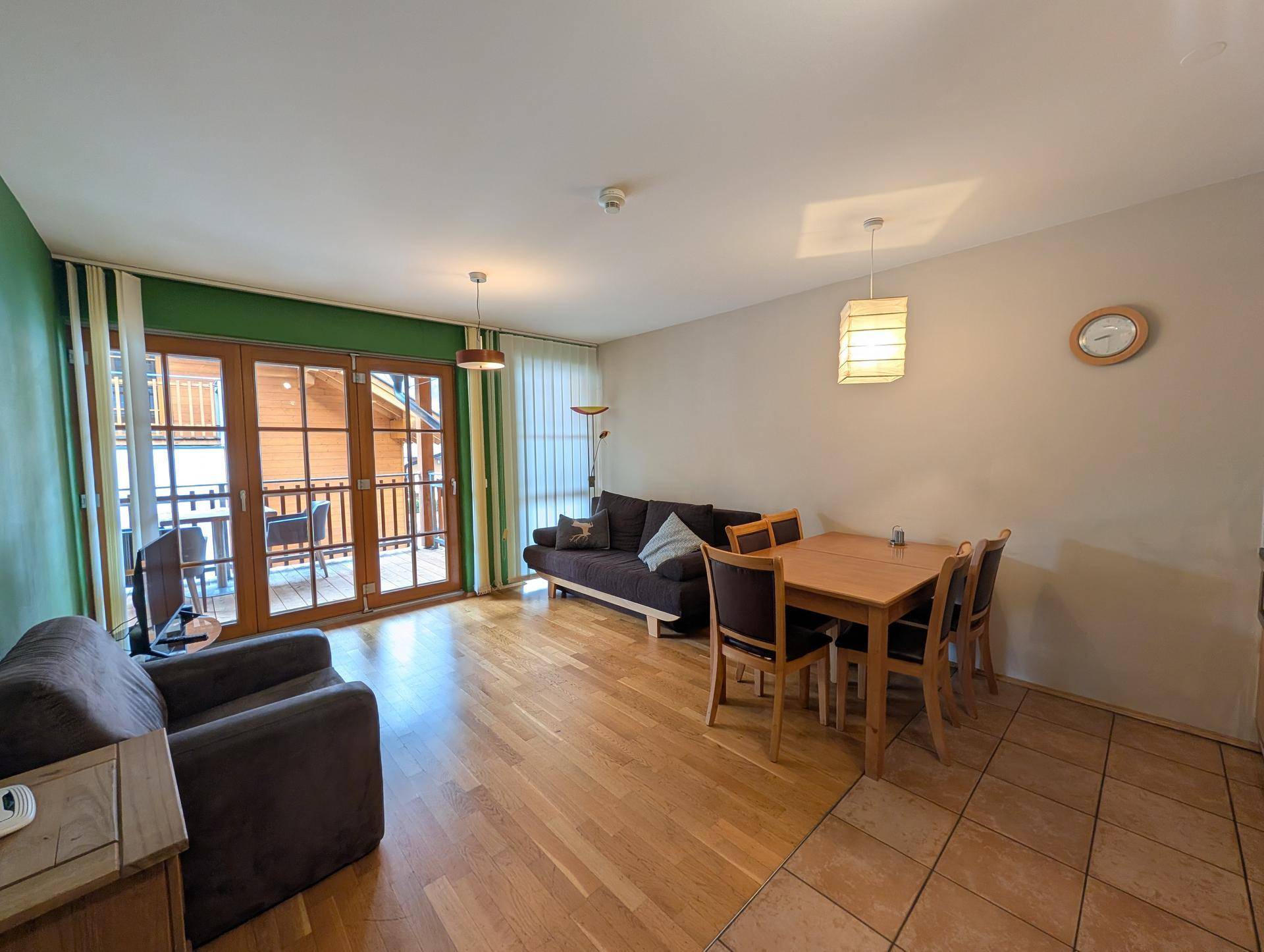 Gemütlicher Wohn- und Essbereich mit Holzboden und Zugang zu einem Balkon, ideal für entspannte Abende.