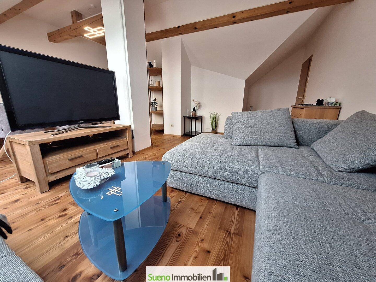 Gemütlicher Wohnbereich mit großem Sofa, Fernseher und Holzboden unter Dachfenstern.