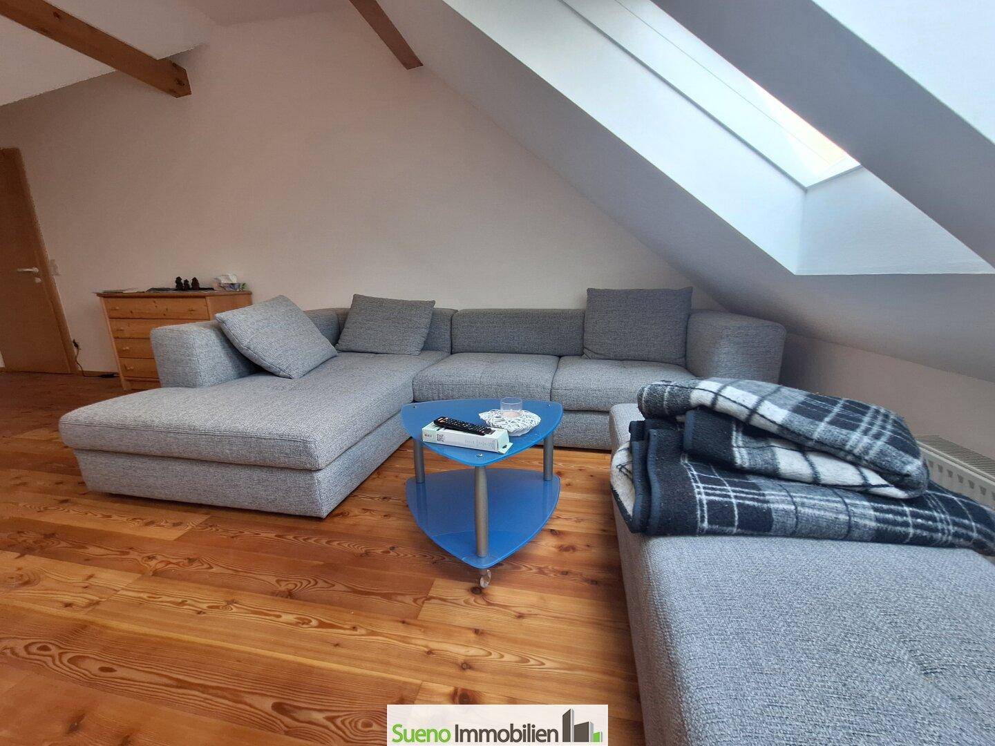 Heller Wohnbereich mit bequemer Couch, Holzboden und schrägen Wänden unter Dachfenstern.