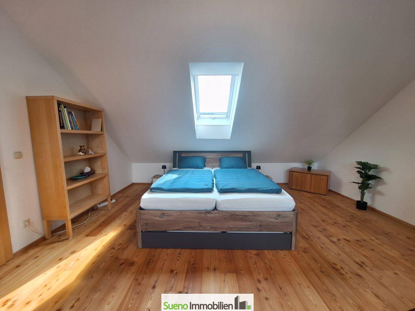 Schlafzimmer mit Doppelbett, Holzboden und einem einzelnen Dachfenster für natürliches Licht.