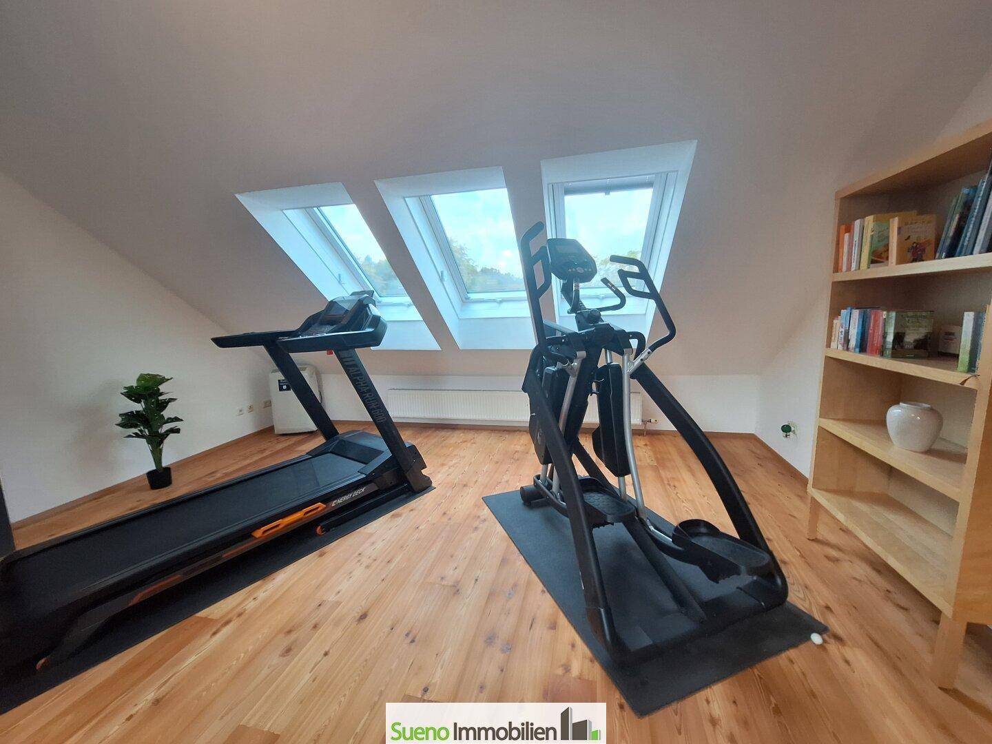 Fitnessraum im Dachgeschoss mit Laufband, Crosstrainer und mehreren Dachfenstern.