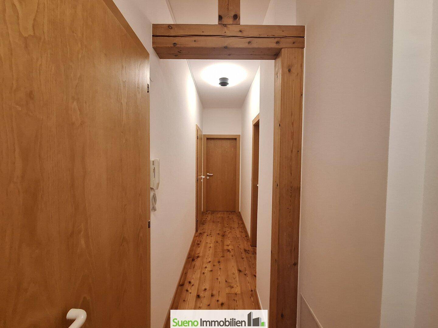 Heller Flur mit Holztüren, Holzboden und einem dekorativen Holzbalken.