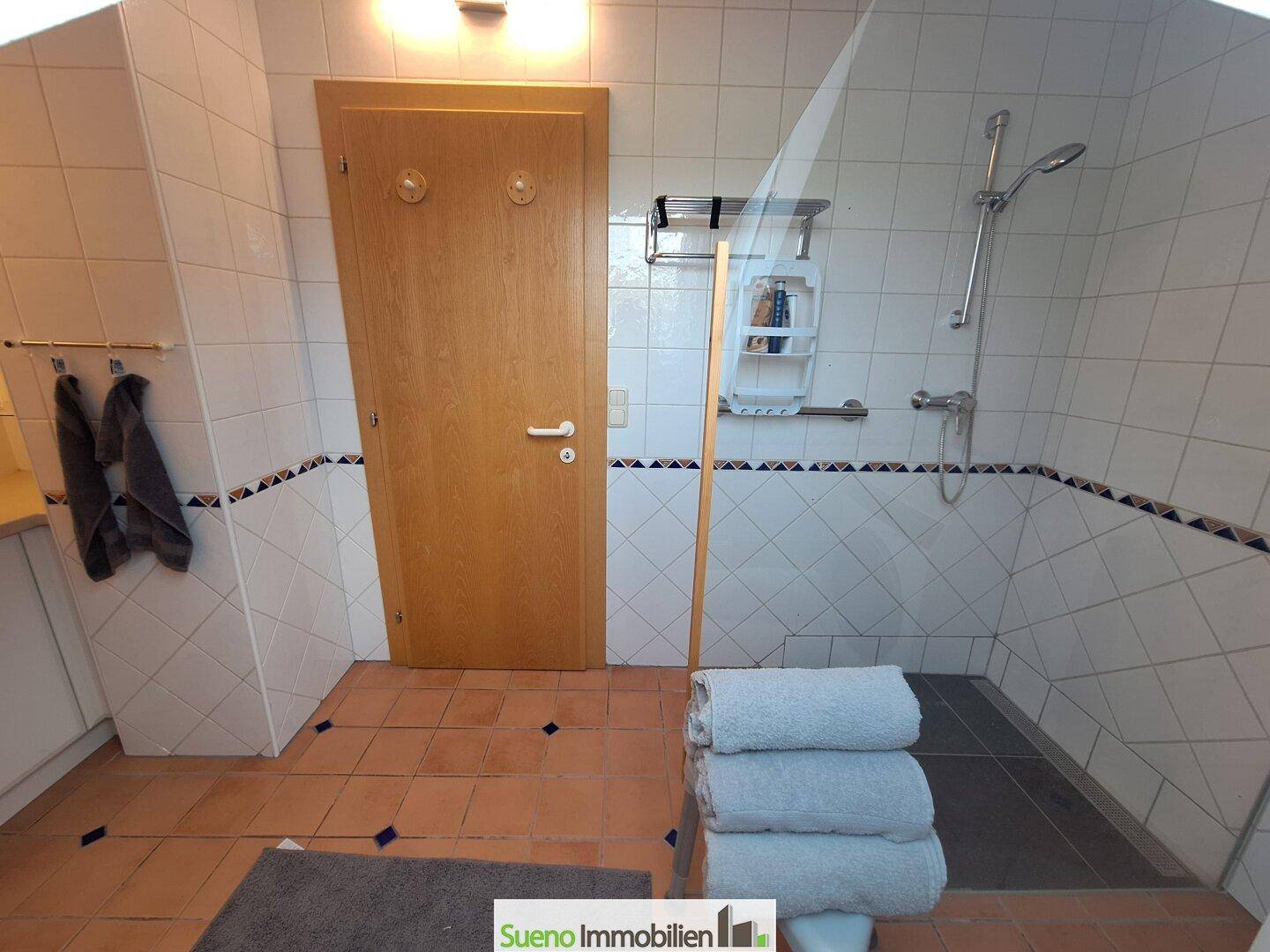 Badezimmer mit ebenerdiger Dusche, terracottafarbenen Fliesen und weißer Wandverkleidung.