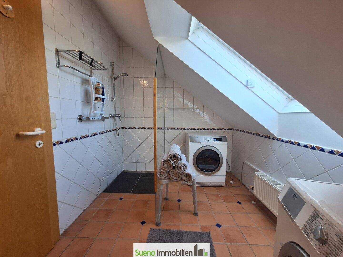 Badezimmer mit Dusche, Waschmaschine, Trockner und Dachfenster für natürliche Belüftung.
