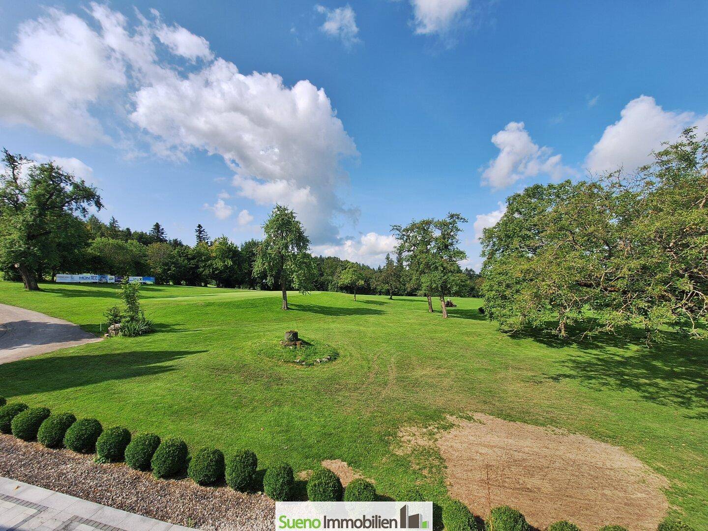 Gepflegter Gartenbereich mit Hecken und Rasenfläche, angrenzend an den Golfplatz.