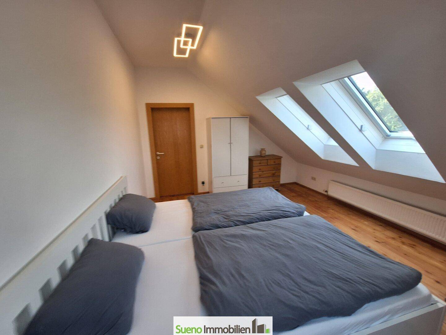 Helles Schlafzimmer im Dachgeschoss mit Doppelbett, Holzboden und modernen Dachfenstern.