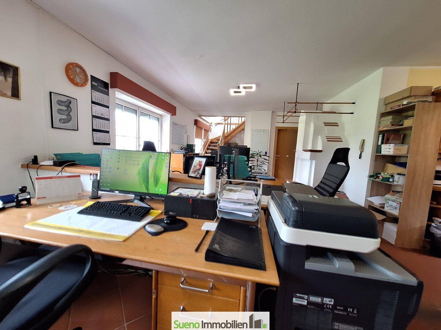 Geräumiges Büro mit mehreren Arbeitsplätzen und einem Treppenaufgang im hinteren Bereich.