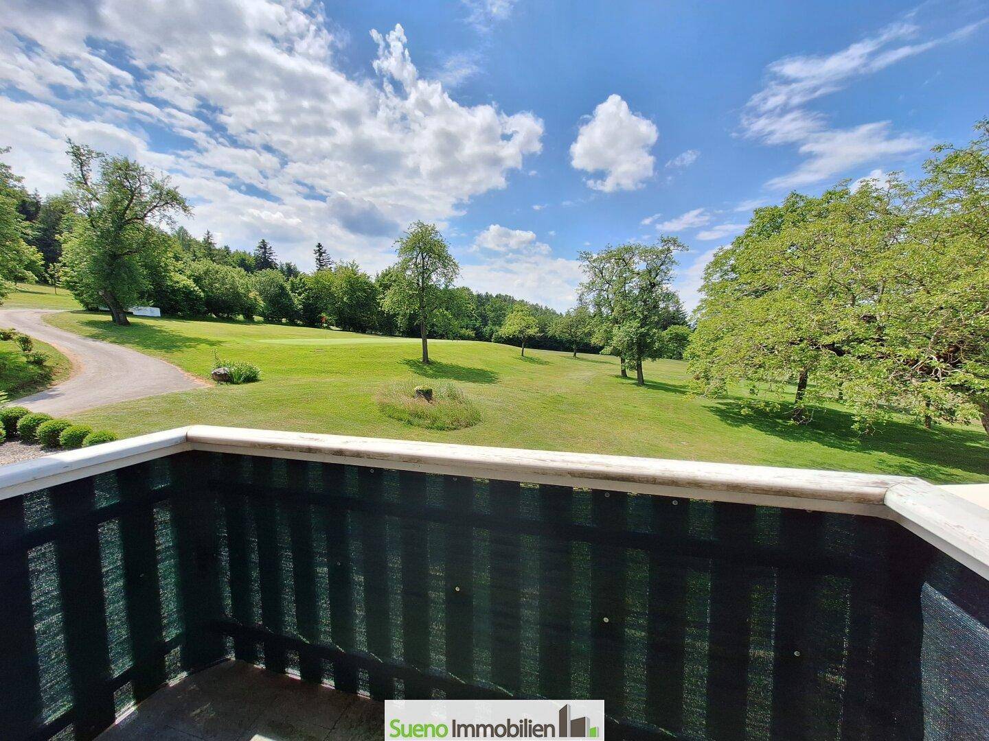 Blick von einem Balkon auf die weitläufige grüne Landschaft des Golfplatzes.