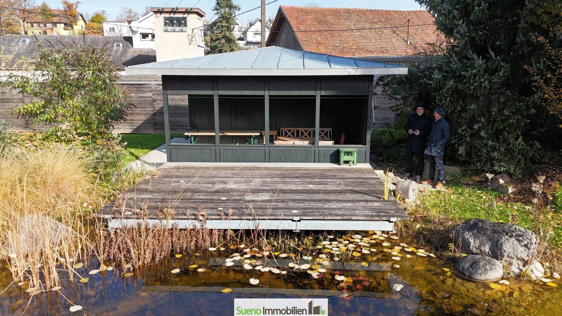 Überdachter Gartenpavillon mit Sitzgelegenheiten am Ufer des Schwimmteichs, ideal für gesellige Stunden.