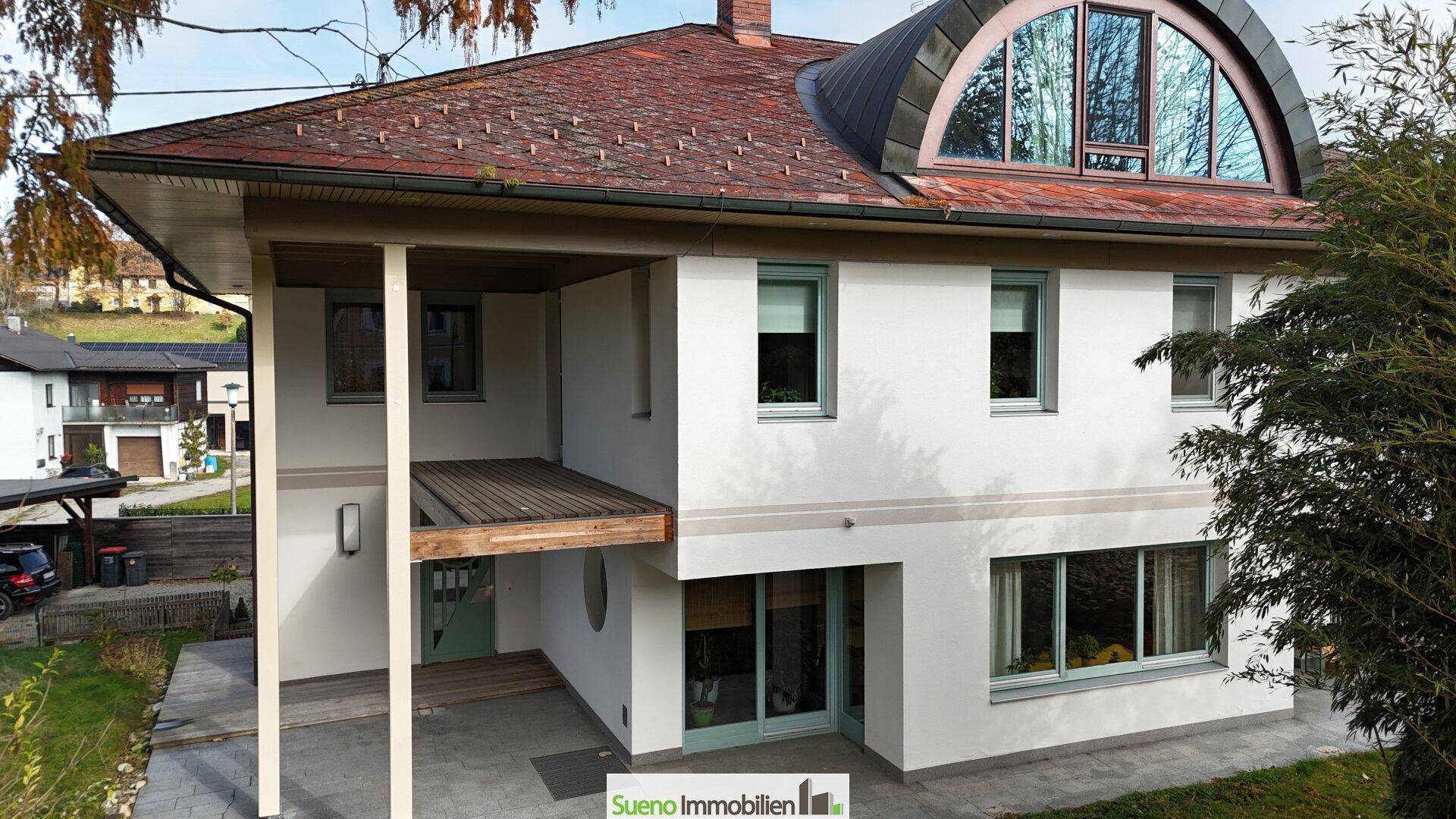 Moderne Hausfassade mit großen Fenstern und einem markanten Rundbogenfenster im Dachgeschoss.