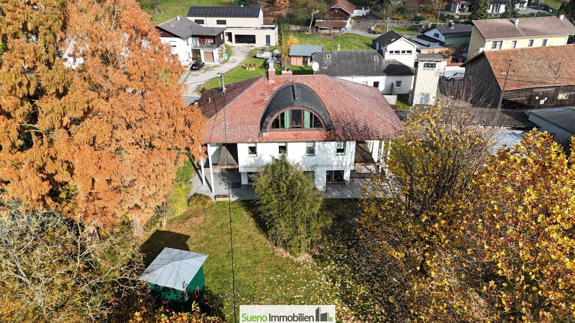 Vogelperspektive des Hauses mit weitläufigem Garten und herbstlicher Baumkulisse in der Nachbarschaft.