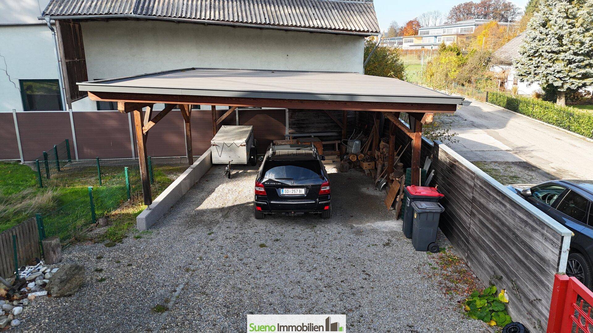 Geräumiger Carport mit Holzbalkenkonstruktion bietet Schutz für Fahrzeuge und Lagerfläche.
