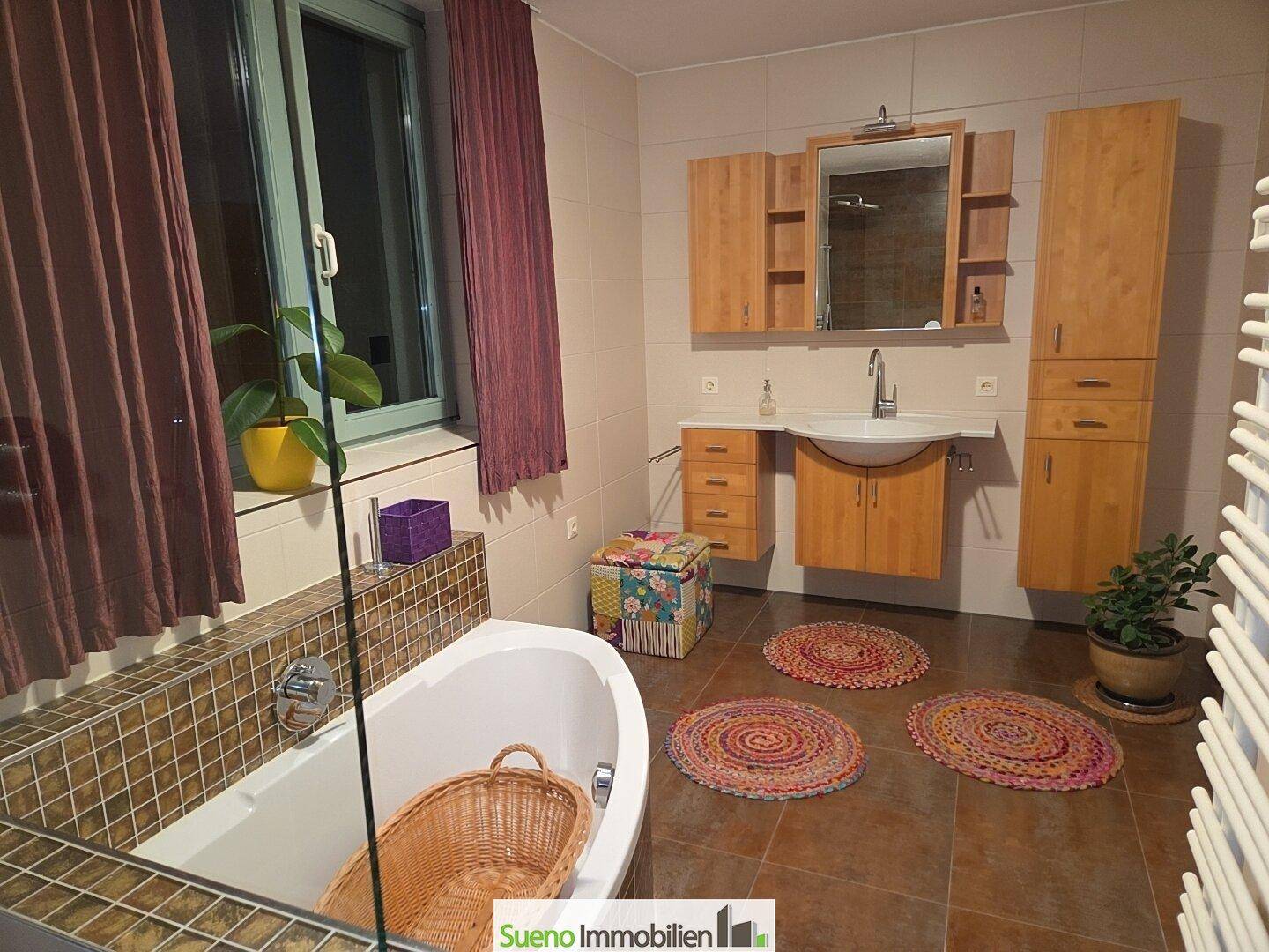 Badezimmer mit Badewanne, Holzmöbeln, Fliesenboden und Fenster.