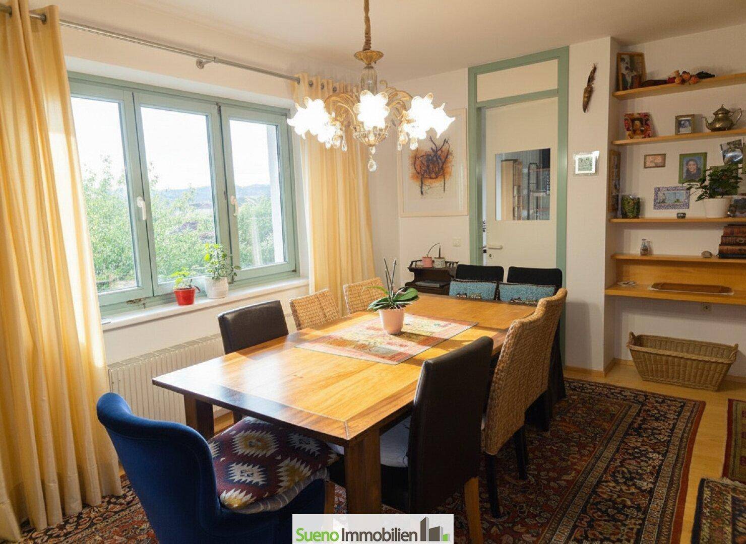 Gemütlicher Essbereich mit großem Holztisch, Kronleuchter und Blick ins Grüne.