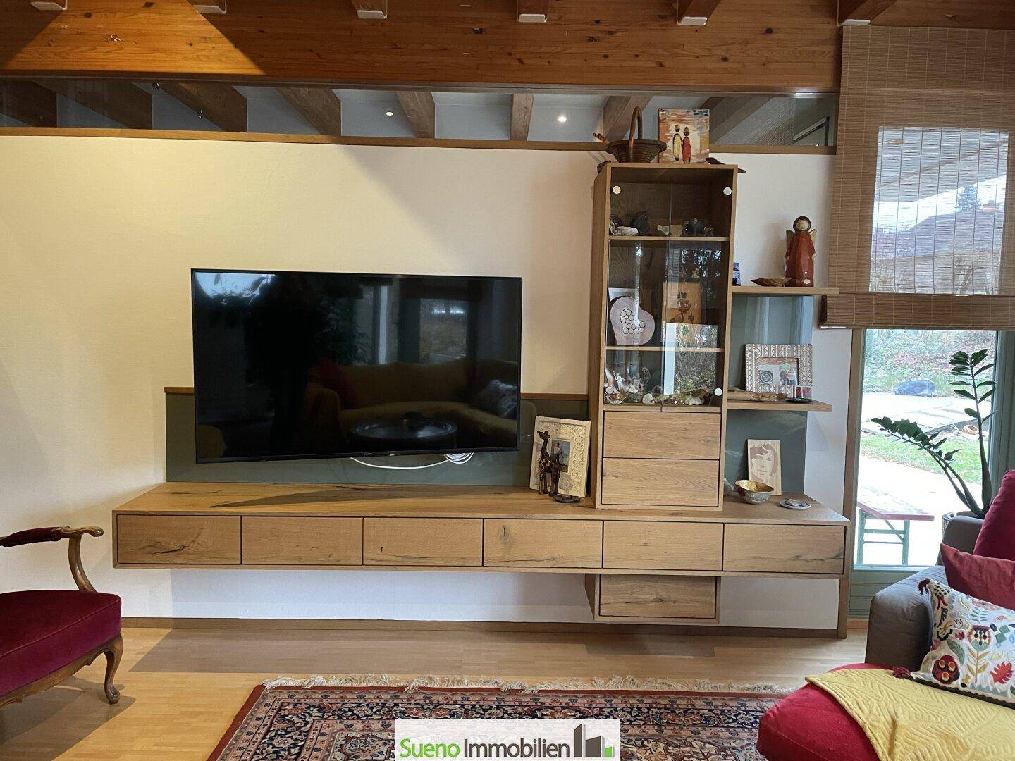 Wohnzimmer mit Holzbalkendecke, großem Fernseher und modernem Sideboard.