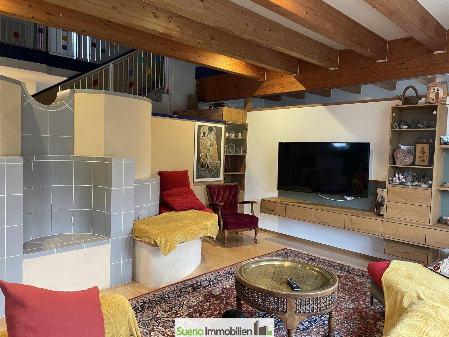 Geräumiges Wohnzimmer mit Holzbalkendecke, Kachelofen und Fernseher.