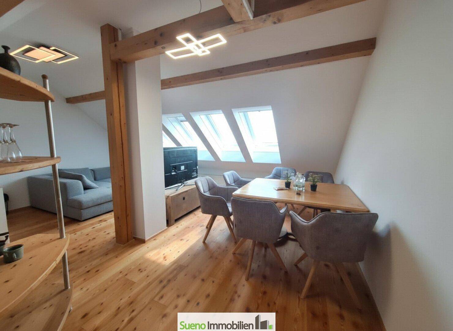 Essbereich mit Holztisch und Stühlen, umgeben von Holzbalken und Dachfenstern.