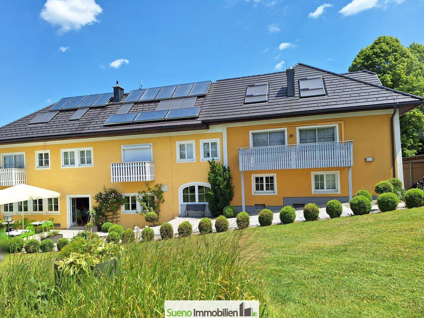 Ansicht des Gebäudes mit gelber Fassade, Solaranlage auf dem Dach und mehreren Balkonen.