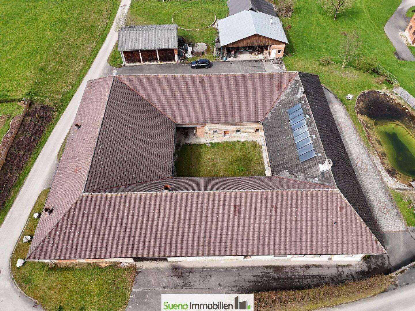 Dachansicht des U-förmigen Bauernhauses mit großem Innenhof und umliegenden Feldern.