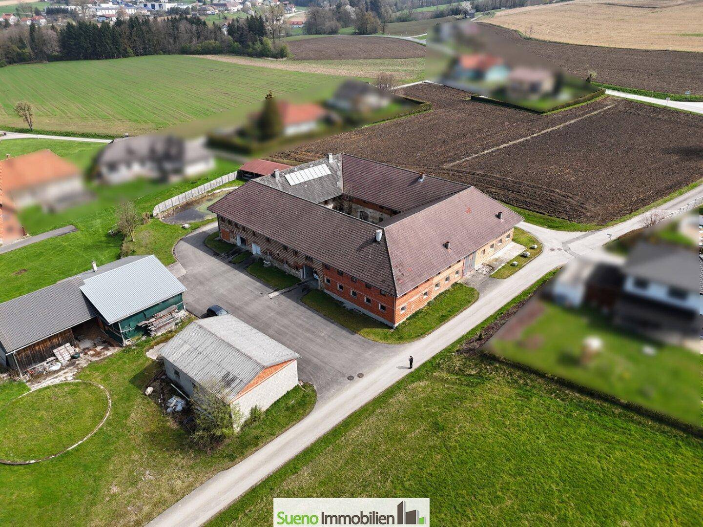 Luftaufnahme des gesamten Anwesens mit Hauptgebäude, Nebengebäuden und weiten Feldern.