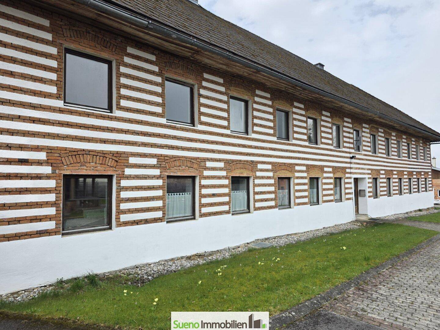 Detailansicht der traditionellen Fassade des Bauernhauses mit charakteristischen Ziegel- und Putzstreifen.