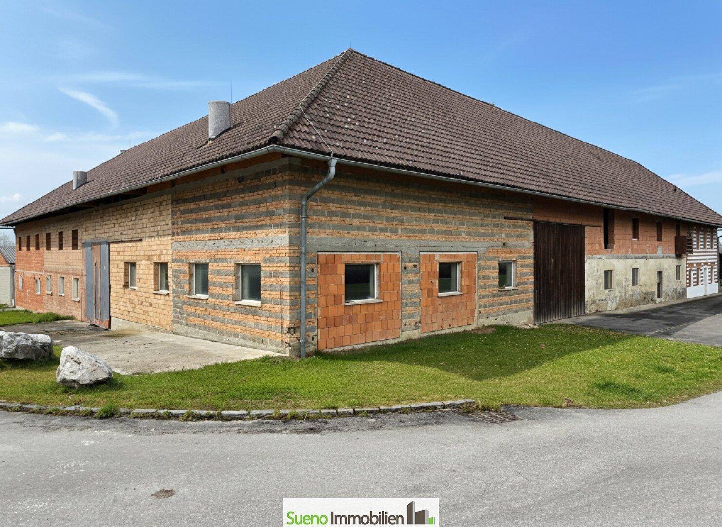 Rückseite des Bauernhauses mit unverputzten Ziegelwänden und verschiedenen Fensteröffnungen.