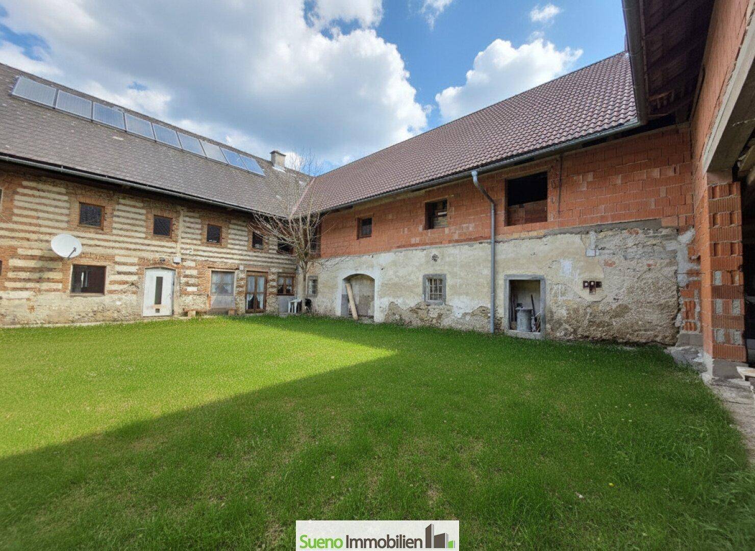 Grüner Innenhof des Bauernhauses mit sonniger Rasenfläche und historischen Gebäudeteilen.