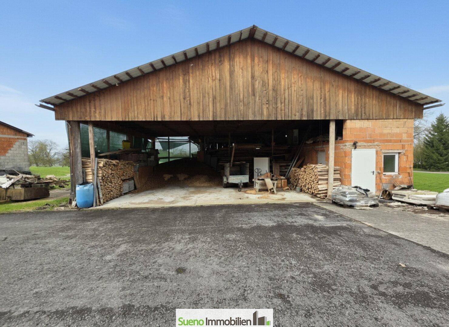 Offener Holzschuppen oder Scheune mit gelagertem Brennholz und landwirtschaftlicher Nutzung.