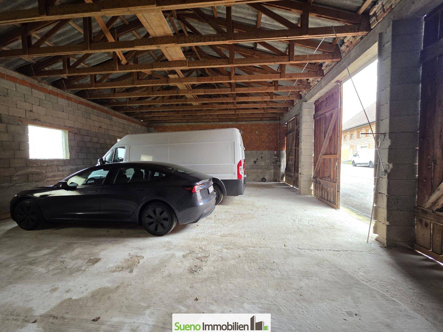 Geräumige Garage mit Betonboden, Platz für mehrere Fahrzeuge und Holztoren.