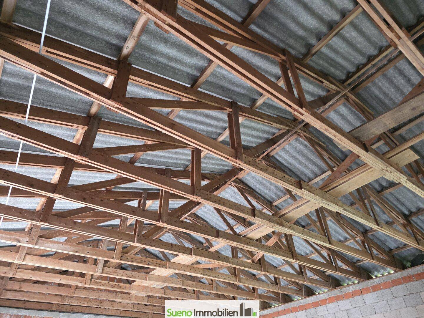Offene Dachkonstruktion aus Holz mit sichtbaren Balken und Wellblechdach.
