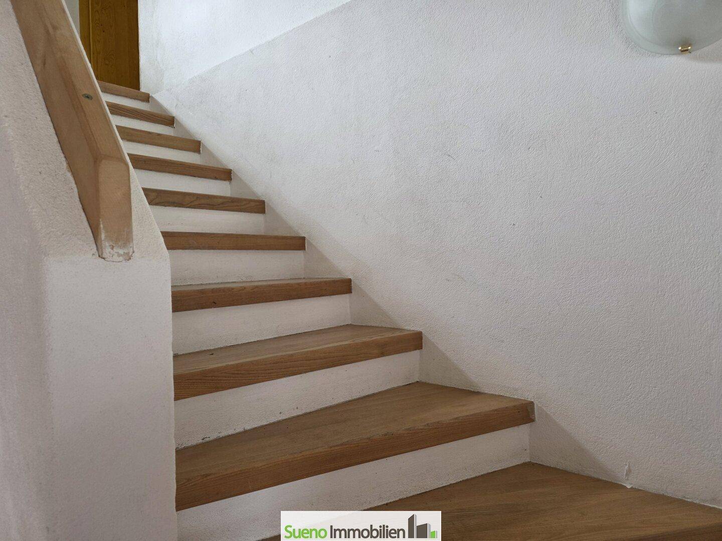 Holztreppe mit weiß gestrichenen Wänden, die in die oberen Stockwerke führt.