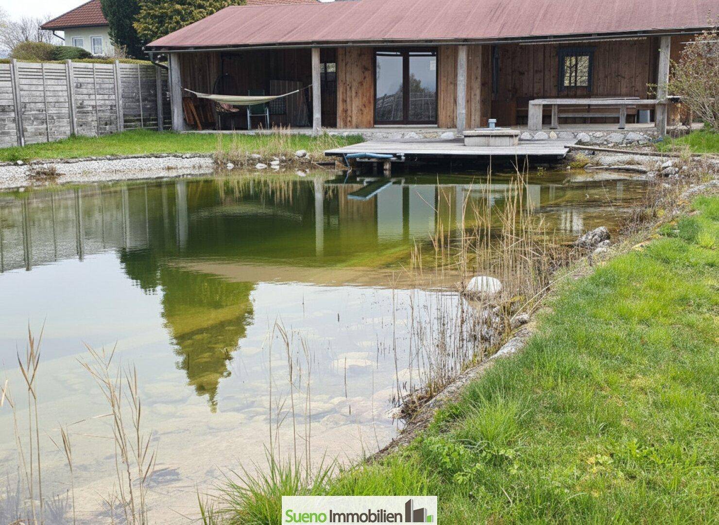 Holzhaus mit überdachtem Außenbereich und einem natürlichen Teich im Vordergrund.