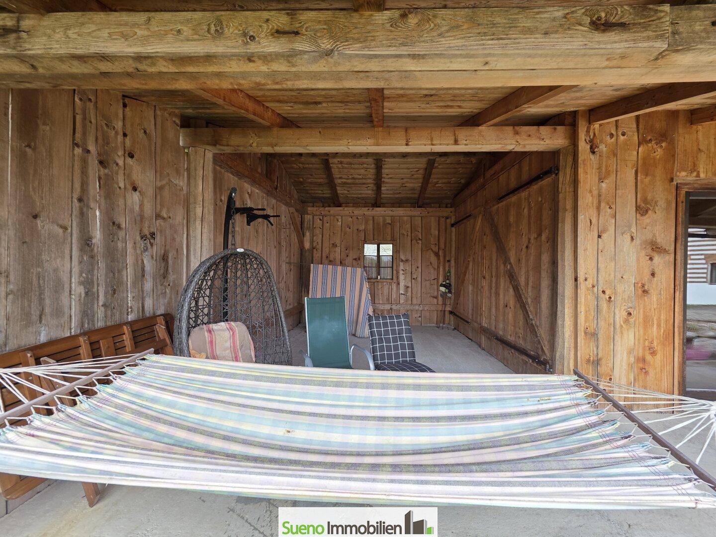 Rustikaler überdachter Außenbereich aus Holz mit Hängematte und Sitzgelegenheiten.