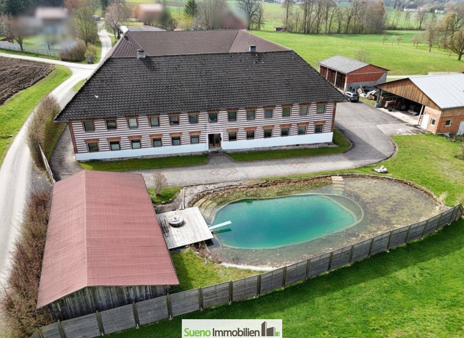Luftaufnahme des Anwesens mit großem Bauernhaus, Nebengebäuden und einem Teich in ländlicher Umgebung.