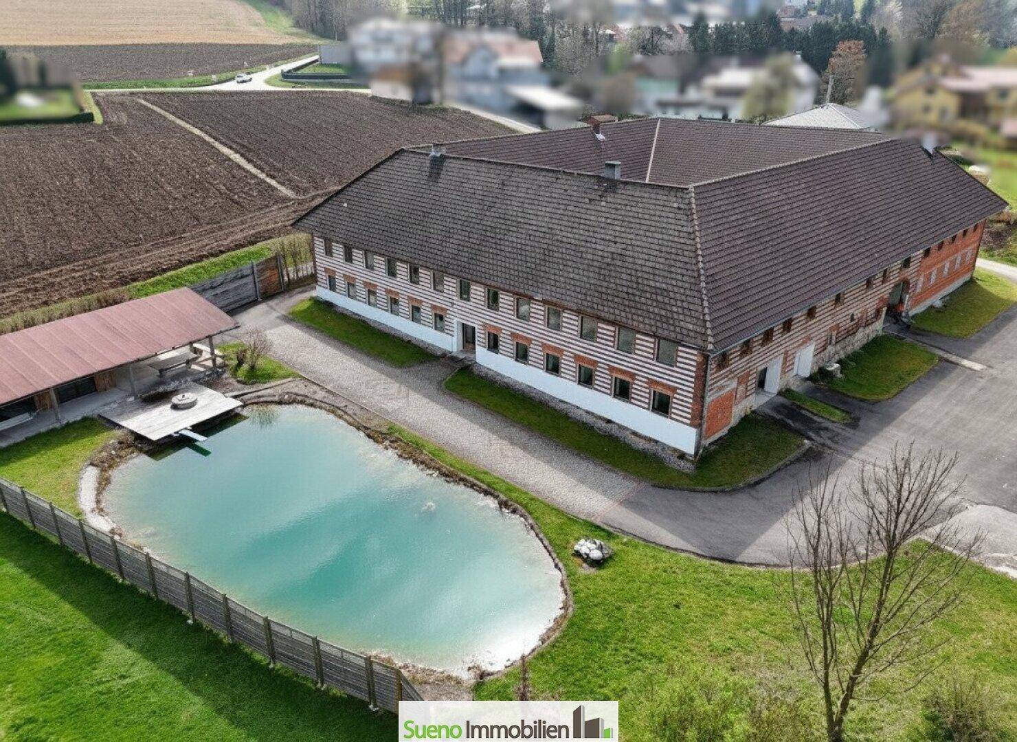 Luftaufnahme des Bauernhauses mit Teich und Nebengebäuden, eingebettet in die ländliche Umgebung.