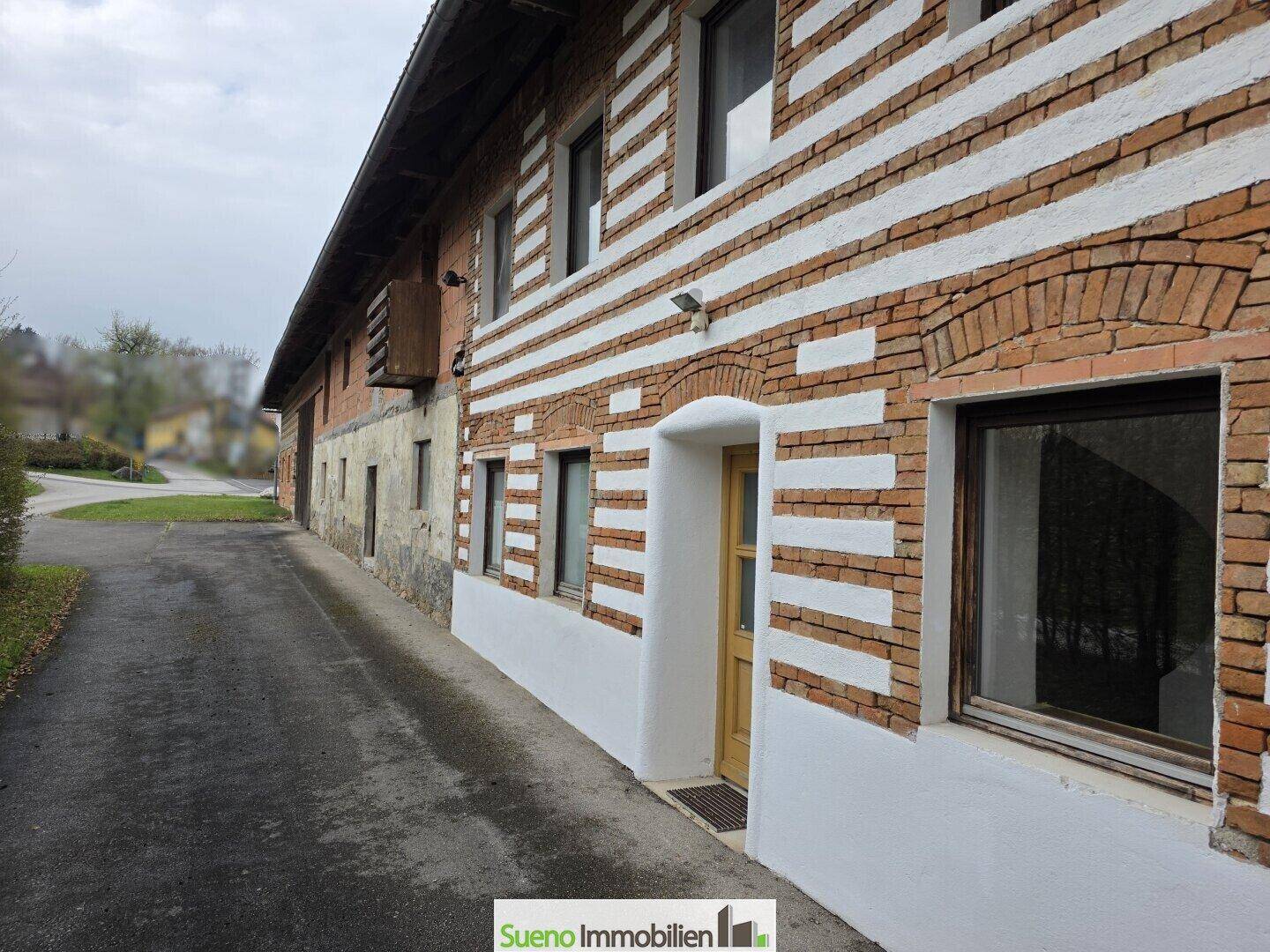 Seitenansicht des Bauernhauses mit traditioneller Fassade, Eingangstür und gepflastertem Weg.